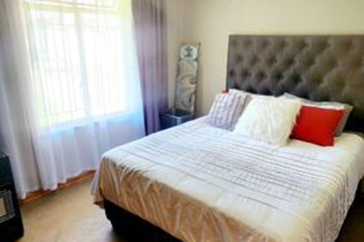 A standard bedroom featuring carpeted flooring, a window with security bars, and a central ceiling light fixture.