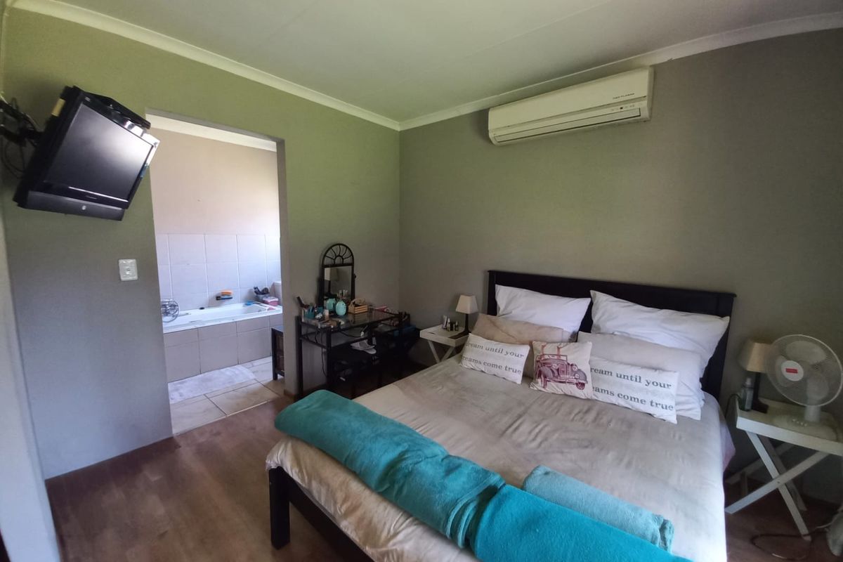 Spacious bedroom featuring laminate flooring, a wall-mounted air conditioning unit, and direct access to an en-suite bathroom.