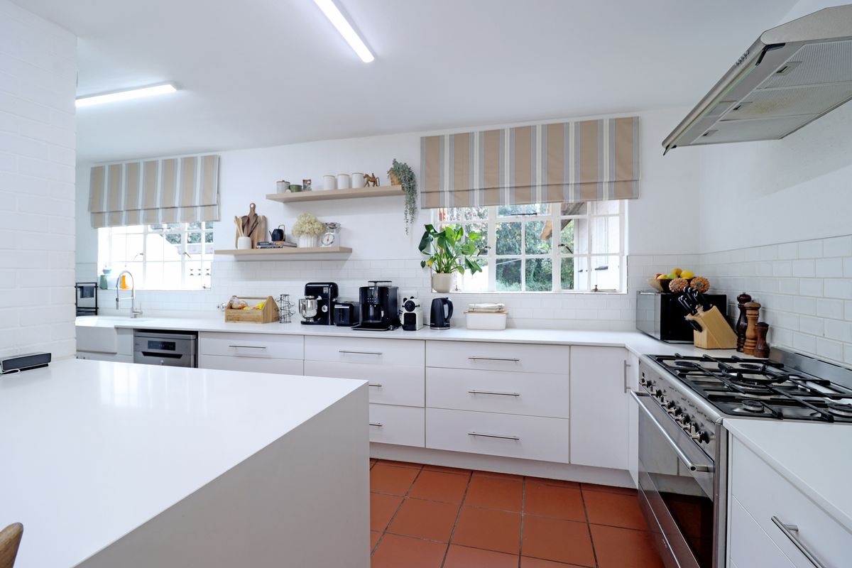 A bright, modern kitchen featuring white cabinetry, quartz countertops, a gas range with extractor, subway tile backsplash, and classic terracotta floor tiles.