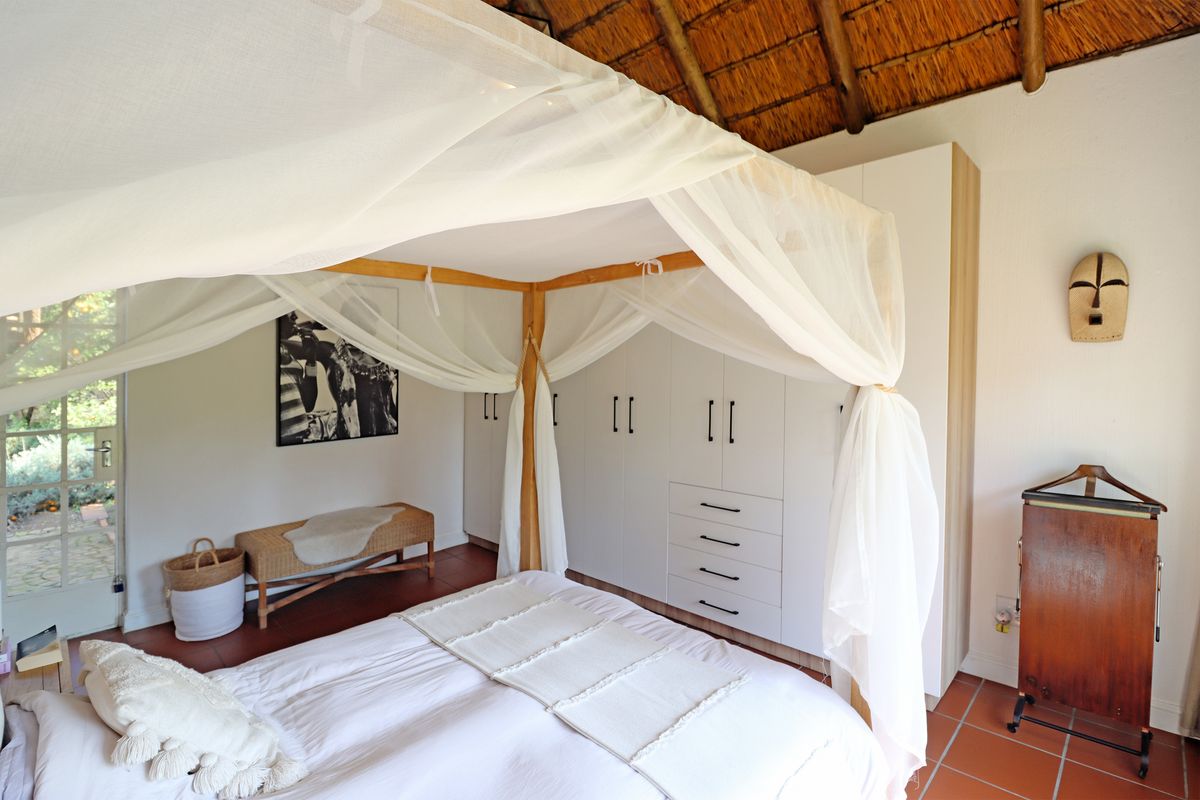 A well-maintained bedroom featuring a high thatched ceiling, built-in cabinetry, terracotta flooring, and direct access to the garden through french doors.