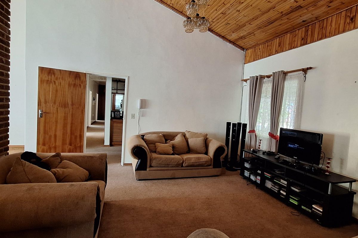 Spacious living room featuring a high vaulted timber ceiling, exposed brickwork, and carpeted flooring, offering a comfortable and traditional living space.