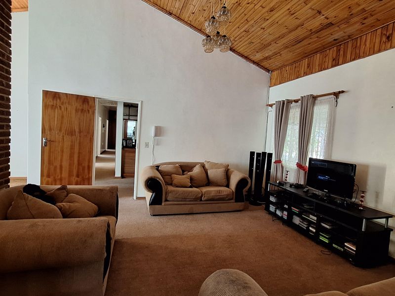 Spacious living room featuring a high vaulted timber ceiling, exposed brickwork, and carpeted flooring, offering a comfortable and traditional living space.