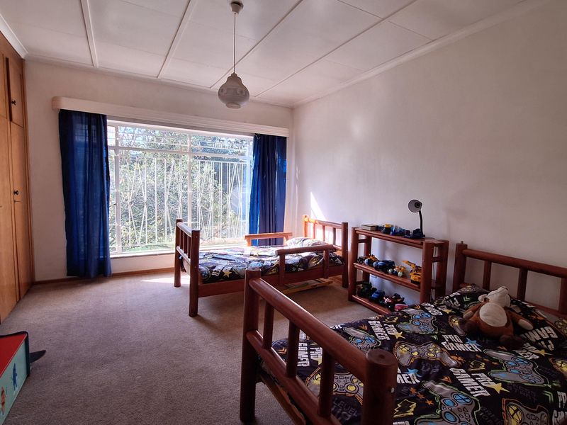A spacious bedroom featuring built-in cupboards, carpeted flooring, and a large window fitted with security bars, providing ample natural light.
