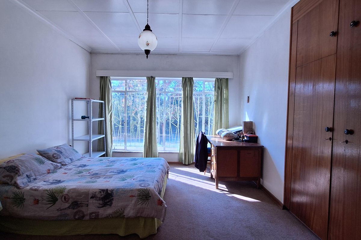 A spacious bedroom featuring built-in wooden wardrobes, carpeted flooring, and a large window with security bars, offering natural light and functional storage space.