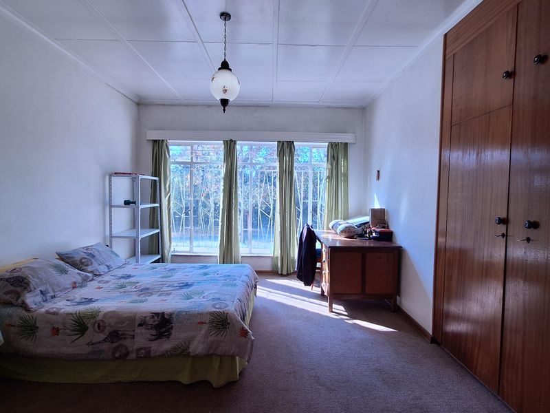 A spacious bedroom featuring built-in wooden wardrobes, carpeted flooring, and a large window with security bars, offering natural light and functional storage space.