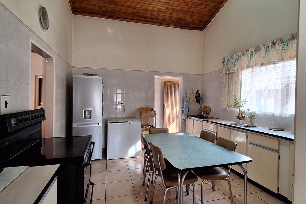 A spacious kitchen featuring a high timber-clad vaulted ceiling, tiled flooring, tiled splashbacks, and functional built-in cabinetry with laminate countertops.