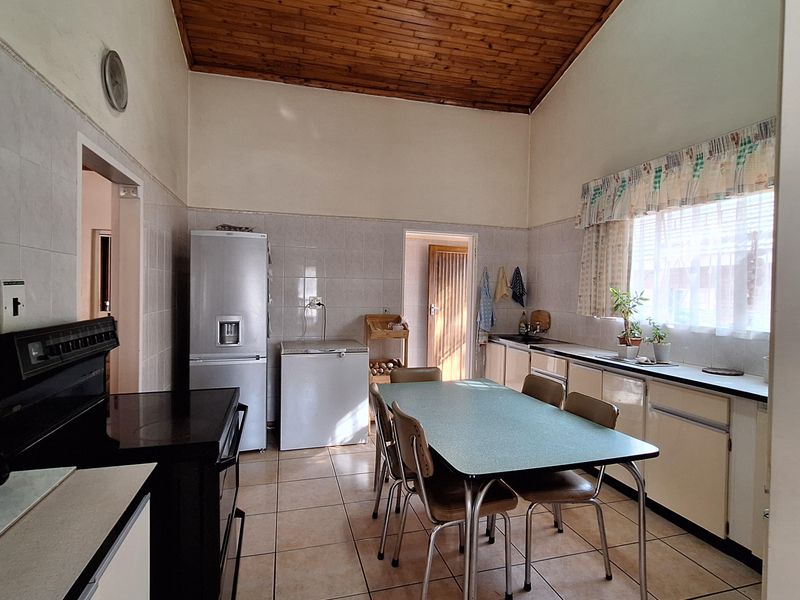 A spacious kitchen featuring a high timber-clad vaulted ceiling, tiled flooring, tiled splashbacks, and functional built-in cabinetry with laminate countertops.