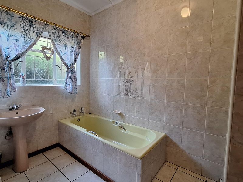 A dated bathroom featuring a pedestal basin and a built-in bathtub with neutral wall and floor tiling.