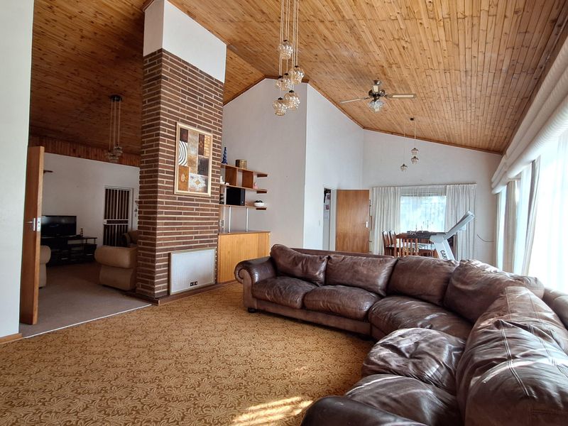 Spacious open-plan living area featuring a vaulted timber ceiling, a prominent brick fireplace column, and built-in shelving, offering a versatile layout.
