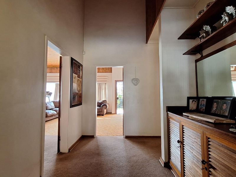A spacious hallway featuring built-in cabinetry, timber ceiling accents, and carpeted flooring, providing access to adjacent living areas.