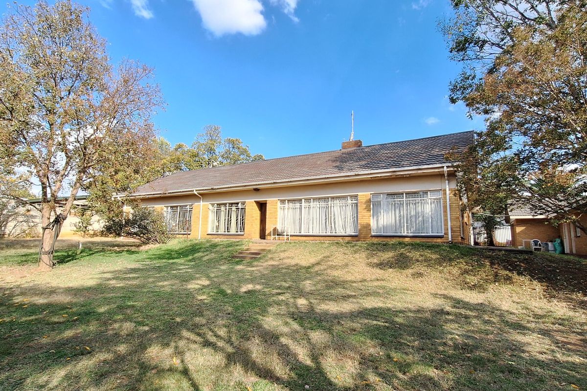 Rear view of a single-story brick house featuring a tiled roof, large windows with security bars, and a spacious garden area.