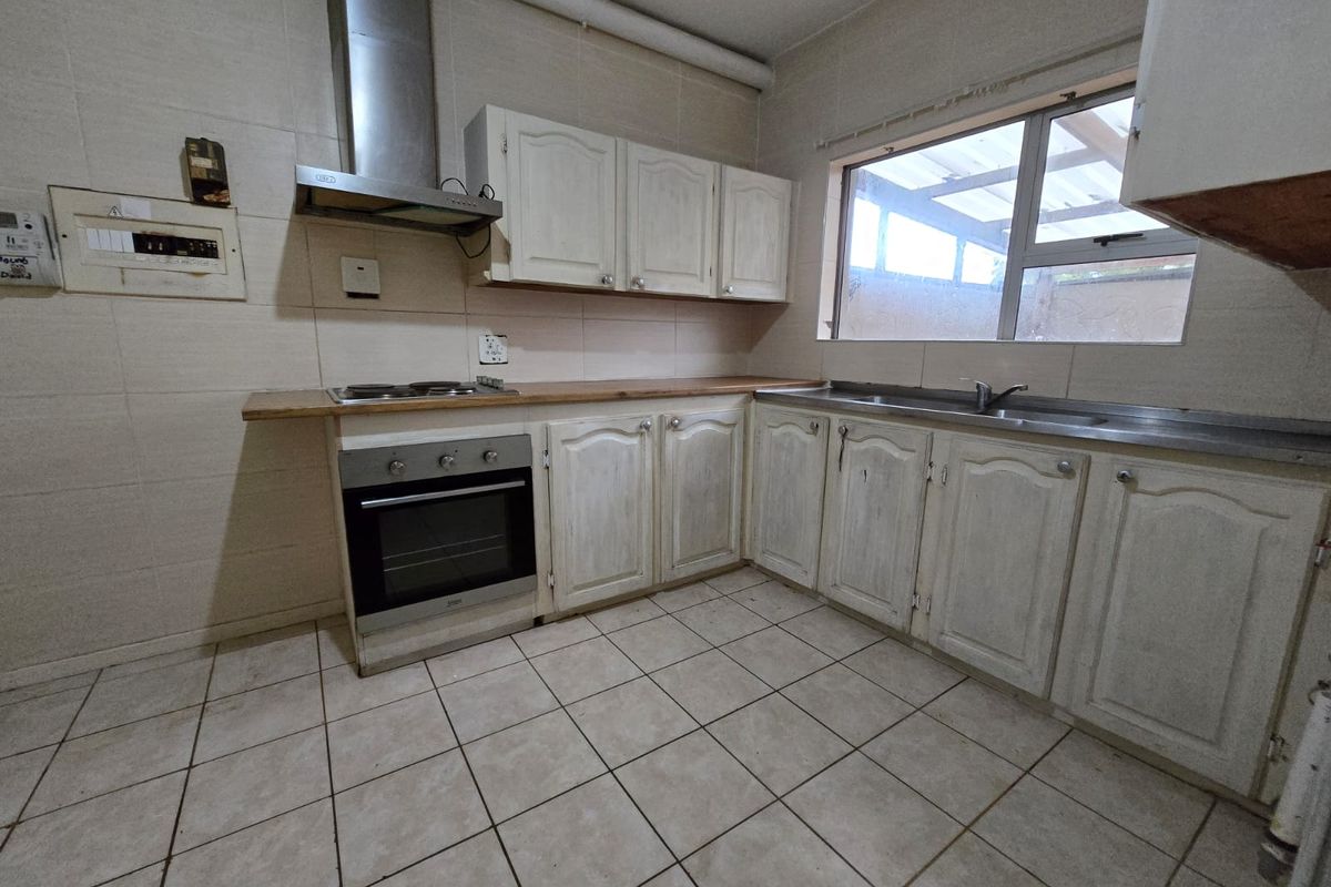A functional kitchen featuring built-in cabinetry, a stainless steel oven and extractor fan, tiled flooring, and a stainless steel sink.