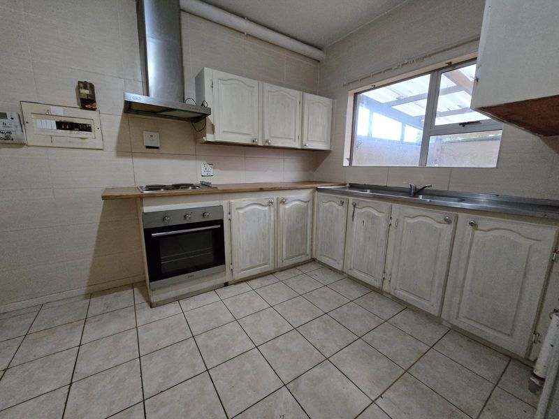 A functional kitchen featuring built-in cabinetry, a stainless steel oven and extractor fan, tiled flooring, and a stainless steel sink.