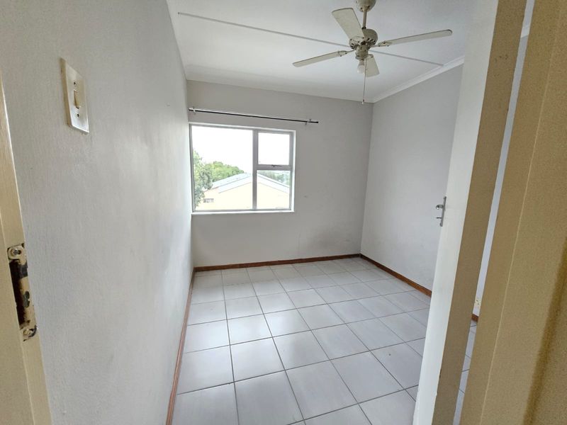 An empty bedroom featuring tiled flooring, a ceiling fan, and a window with natural light, ready for personalization.