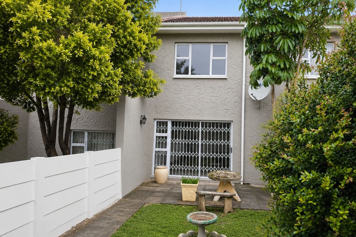 Rear view of the apartment featuring a paved patio area, security gate, and established garden space.