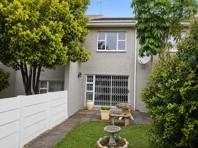 Rear view of the apartment featuring a paved patio area, security gate, and established garden space.