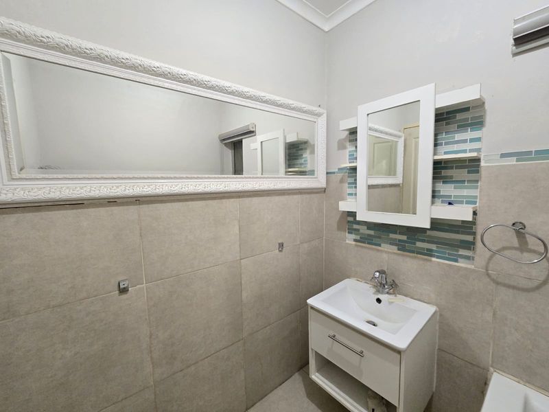 A functional bathroom featuring a modern vanity unit, mosaic tile accents, and a large wall-mounted mirror.