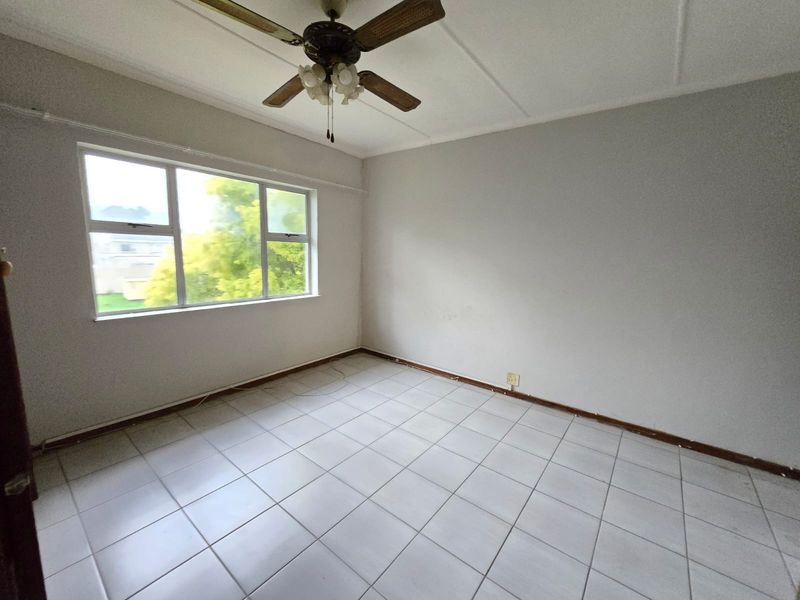A vacant bedroom featuring neutral tiled flooring, a ceiling fan, and large windows providing natural light.