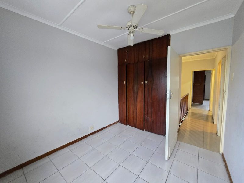 An empty bedroom featuring tiled flooring, a ceiling fan, and built-in wooden cupboards, offering a blank canvas for renovation.