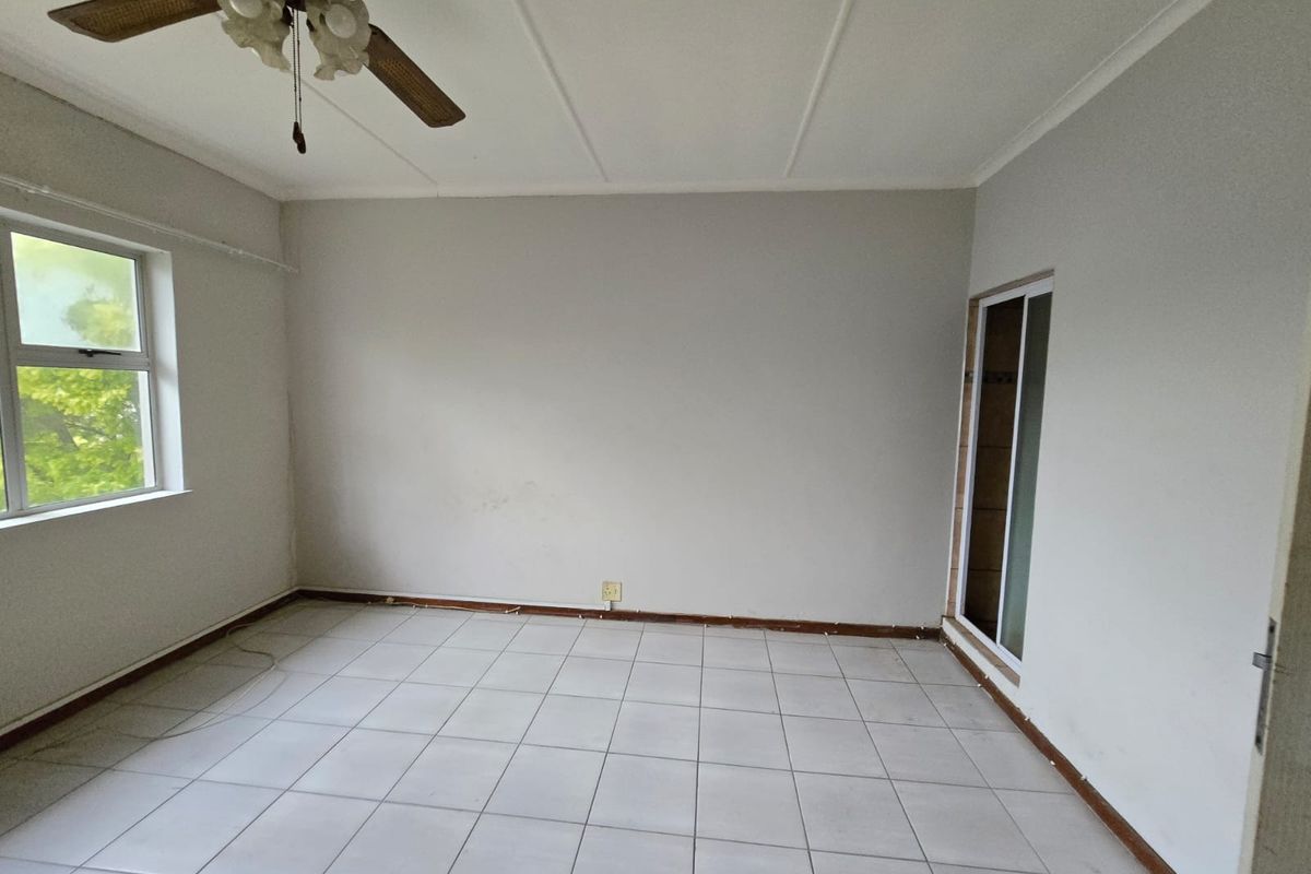An empty bedroom featuring tiled flooring, a ceiling fan, and a sliding door, providing a blank canvas for potential interior design updates.
