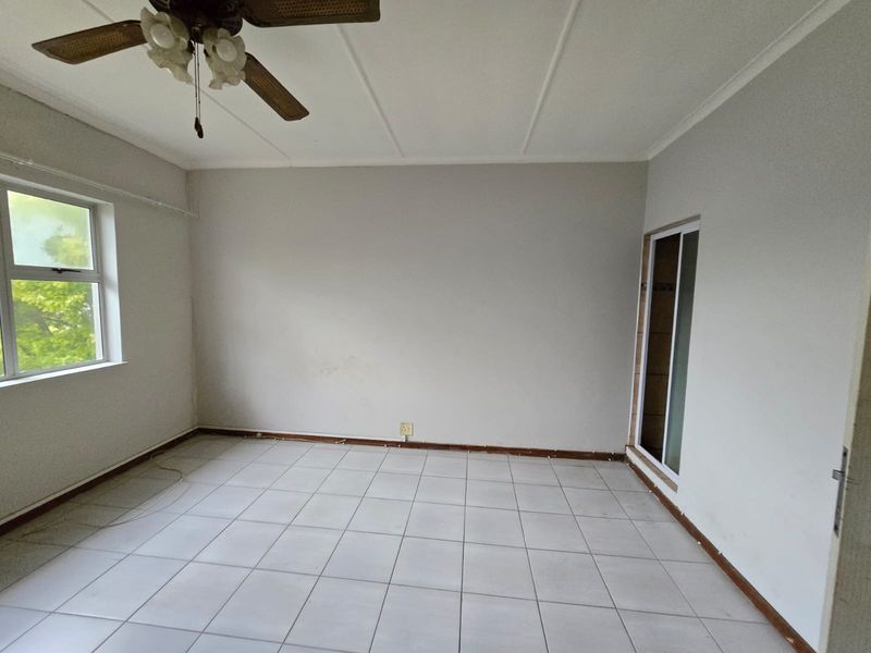An empty bedroom featuring tiled flooring, a ceiling fan, and a sliding door, providing a blank canvas for potential interior design updates.