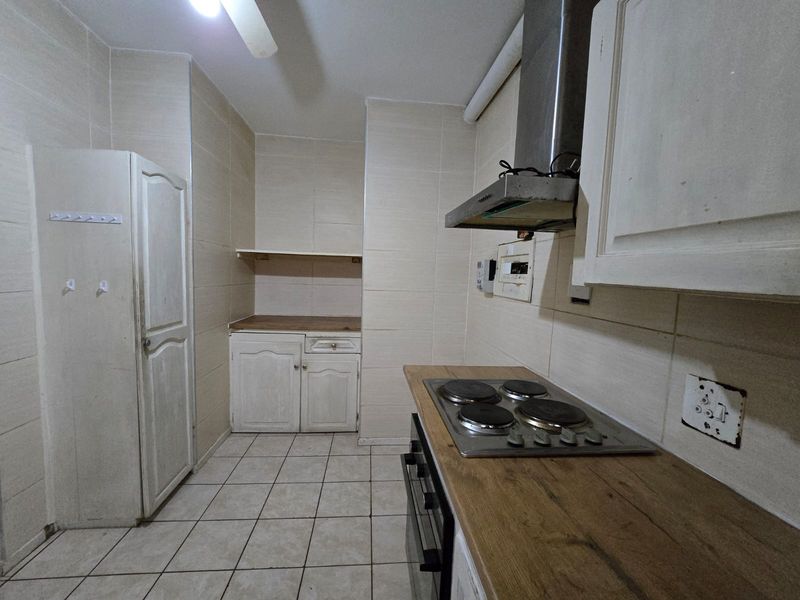 A functional kitchen featuring built-in cabinetry, wooden countertops, an electric hob, and an extractor fan, with tiled walls and flooring throughout.