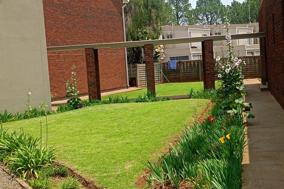 A well-maintained rear garden area featuring a manicured lawn, established flower beds, and a brick-columned pergola structure.