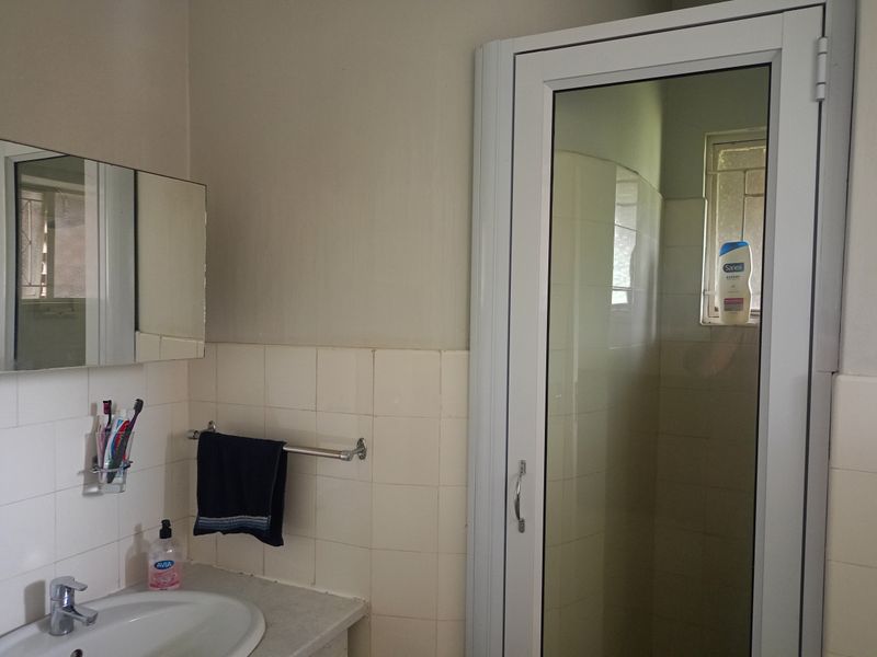 A functional bathroom featuring a vanity basin, wall-mounted mirror, and a separate shower enclosure with an aluminum frame.
