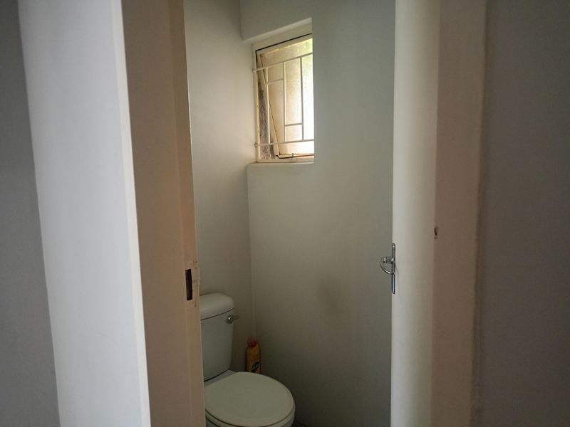 A compact bathroom featuring a standard toilet and a small window with security bars, viewed from the hallway entrance.