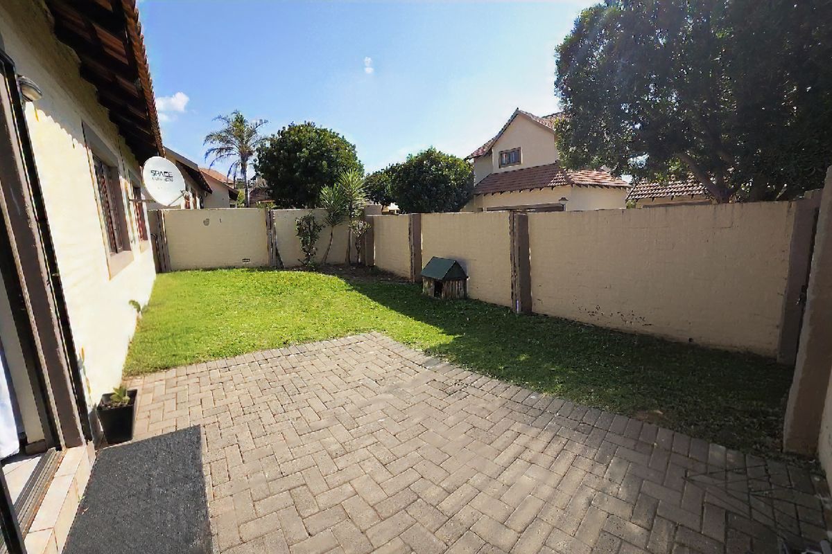 A private rear garden featuring a paved patio area, a small lawn, and high boundary walls for added privacy.