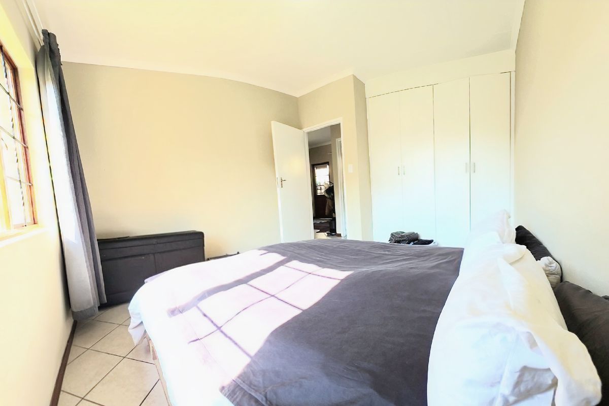 A bedroom featuring built-in cupboards, tiled flooring, and natural light from a large window.