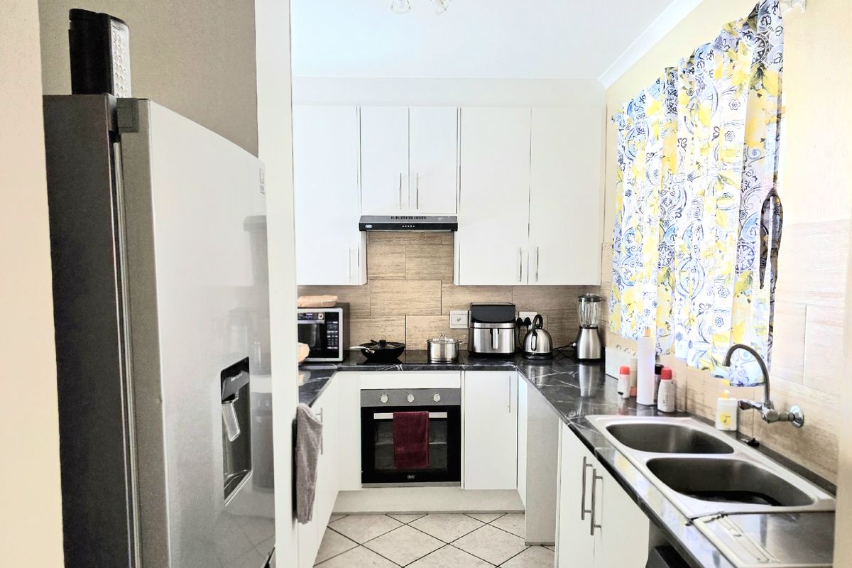 A functional kitchen featuring white cabinetry, dark stone-look countertops, a built-in oven, extractor fan, and a double-basin stainless steel sink.