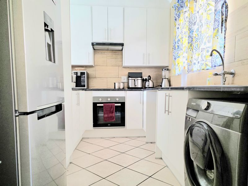 Compact kitchen featuring white cabinetry, dark countertops, built-in oven, extractor fan, and integrated laundry plumbing.