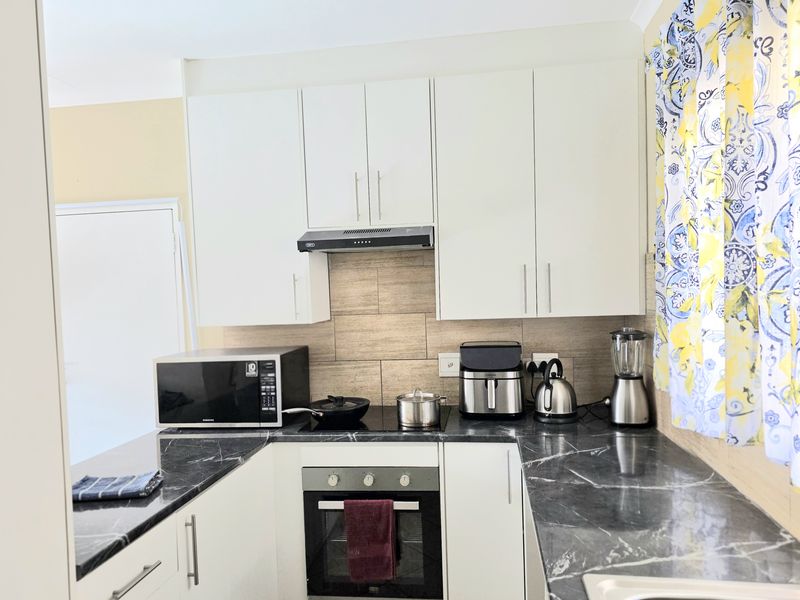 A functional kitchen featuring white cabinetry, dark marble-effect countertops, a built-in oven, and a modern extractor fan with tiled splashback.