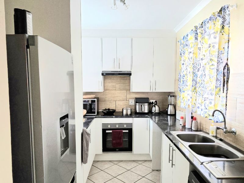 A functional kitchen featuring white cabinetry, dark stone-look countertops, a built-in oven, extractor fan, and a double-basin stainless steel sink.