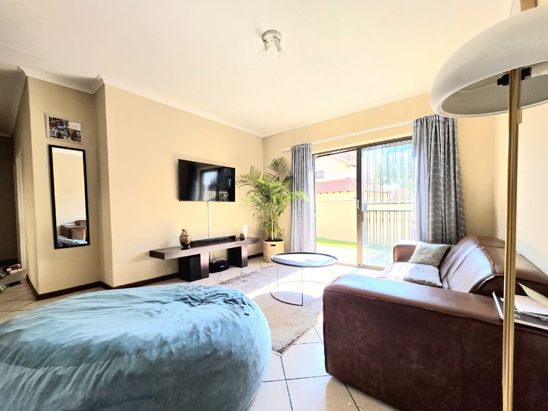 A bright living room featuring tiled flooring, a wall-mounted television, and sliding glass doors that provide direct access to the outdoor area.