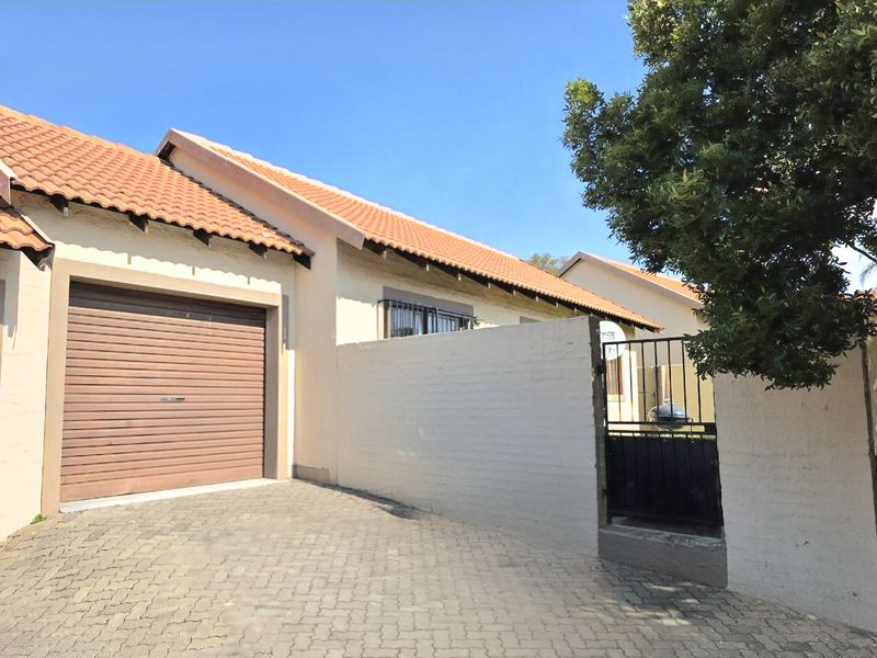Front exterior view of the townhouse featuring a single garage with a roller door, paved driveway, and a gated pedestrian entrance.