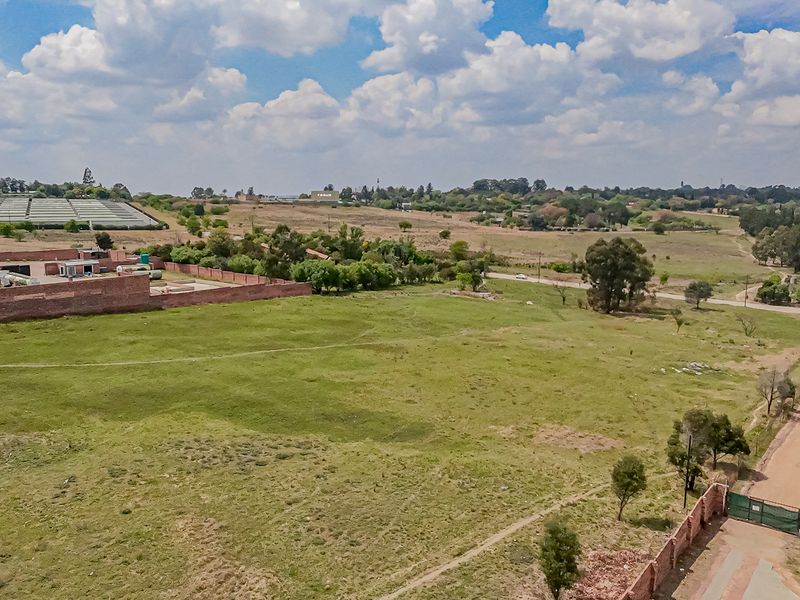 Aerial view of a large, vacant residential plot featuring perimeter brick walling, a gated entrance, and access via an unpaved road.
