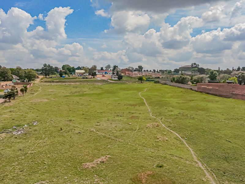 An aerial view of a large, vacant residential plot featuring open grassland and perimeter boundary walls.