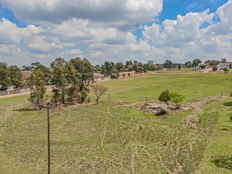 An aerial view of a large, undeveloped residential plot featuring open grassy terrain, mature trees, and existing utility infrastructure.