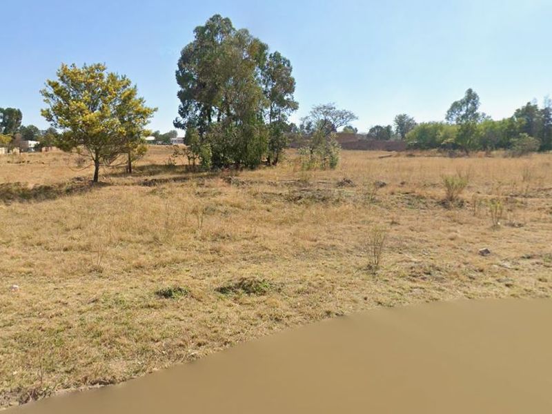 A view of a vacant residential plot featuring open grassland and mature trees, suitable for future development.