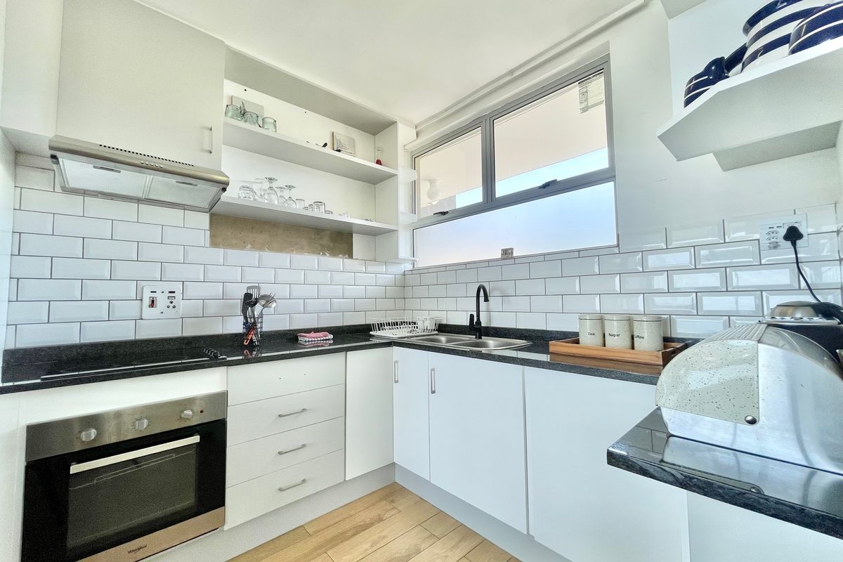 Modern kitchen featuring white cabinetry, subway tile backsplash, dark stone countertops, integrated oven, extractor fan, and wood-look flooring.