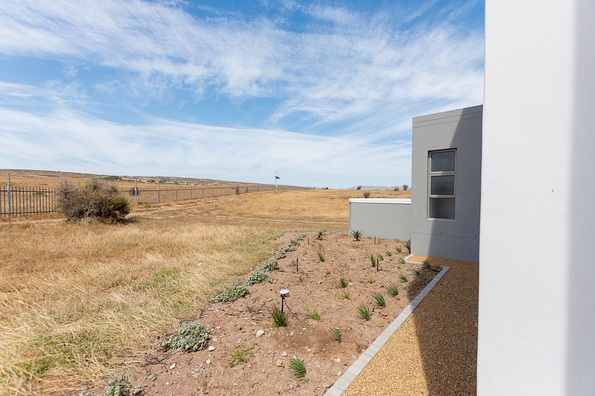 A view of the rear exterior of the property featuring a gravel pathway, a landscaped garden bed, and open field views with perimeter fencing.