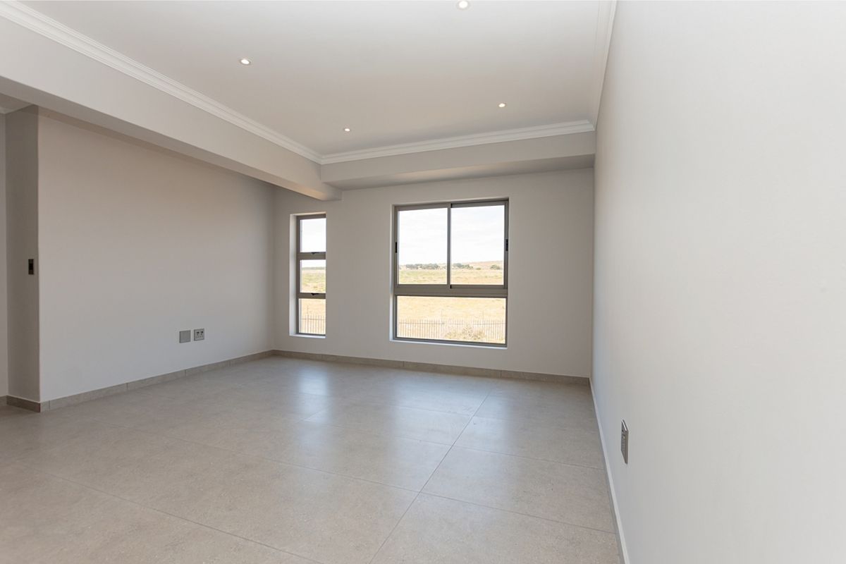 A bright, empty bedroom featuring neutral tiled flooring, recessed downlighting, crown molding, and aluminium-framed windows with a rural view.