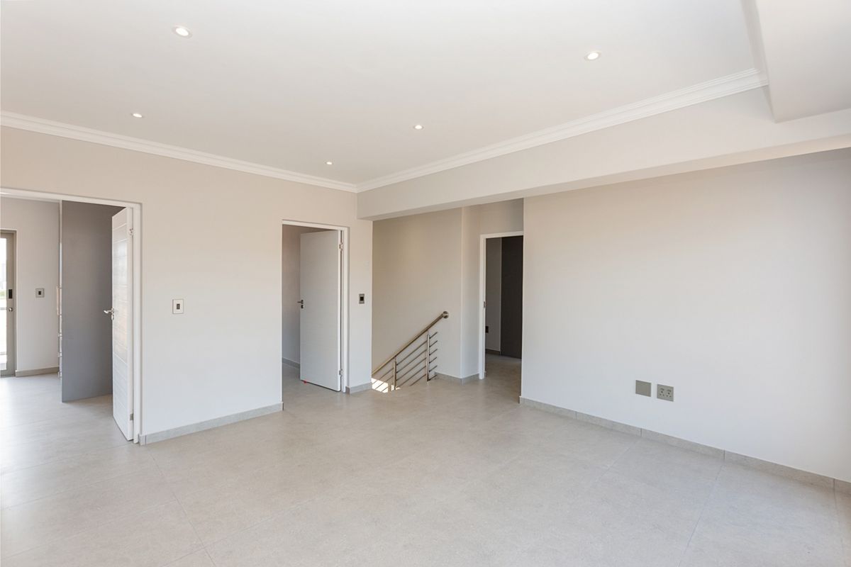 A bright, spacious, and empty living area featuring neutral tiled floors, recessed lighting, and a modern staircase with a metal balustrade.
