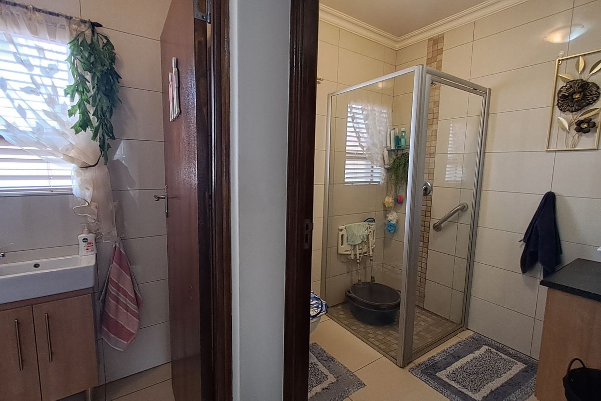 A functional bathroom featuring a vanity unit, tiled walls, and a glass-enclosed shower with a safety grab rail.