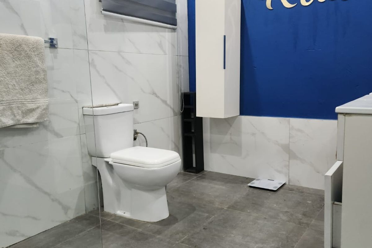 A modern bathroom featuring marble-look wall tiles, grey floor tiles, a wall-mounted storage cabinet, and a standard toilet.