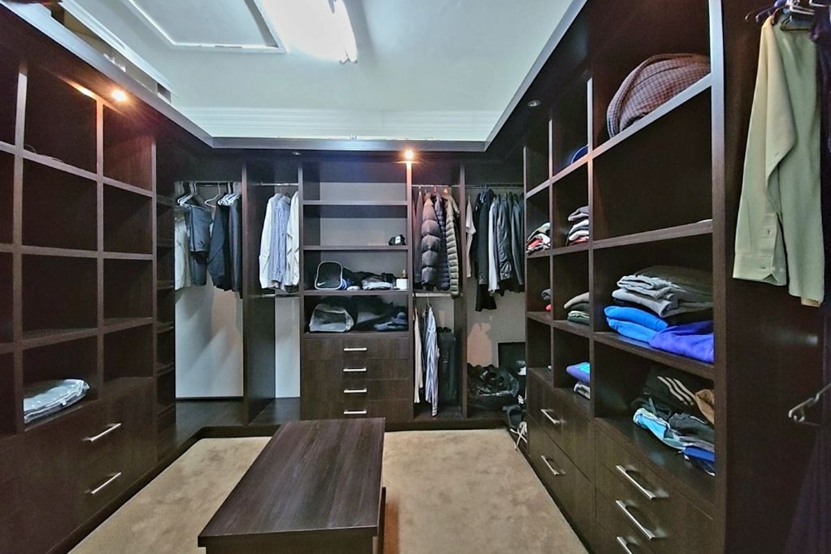 A spacious walk-in dressing room featuring extensive custom dark wood cabinetry, integrated shelving, hanging rails, and built-in drawer units.