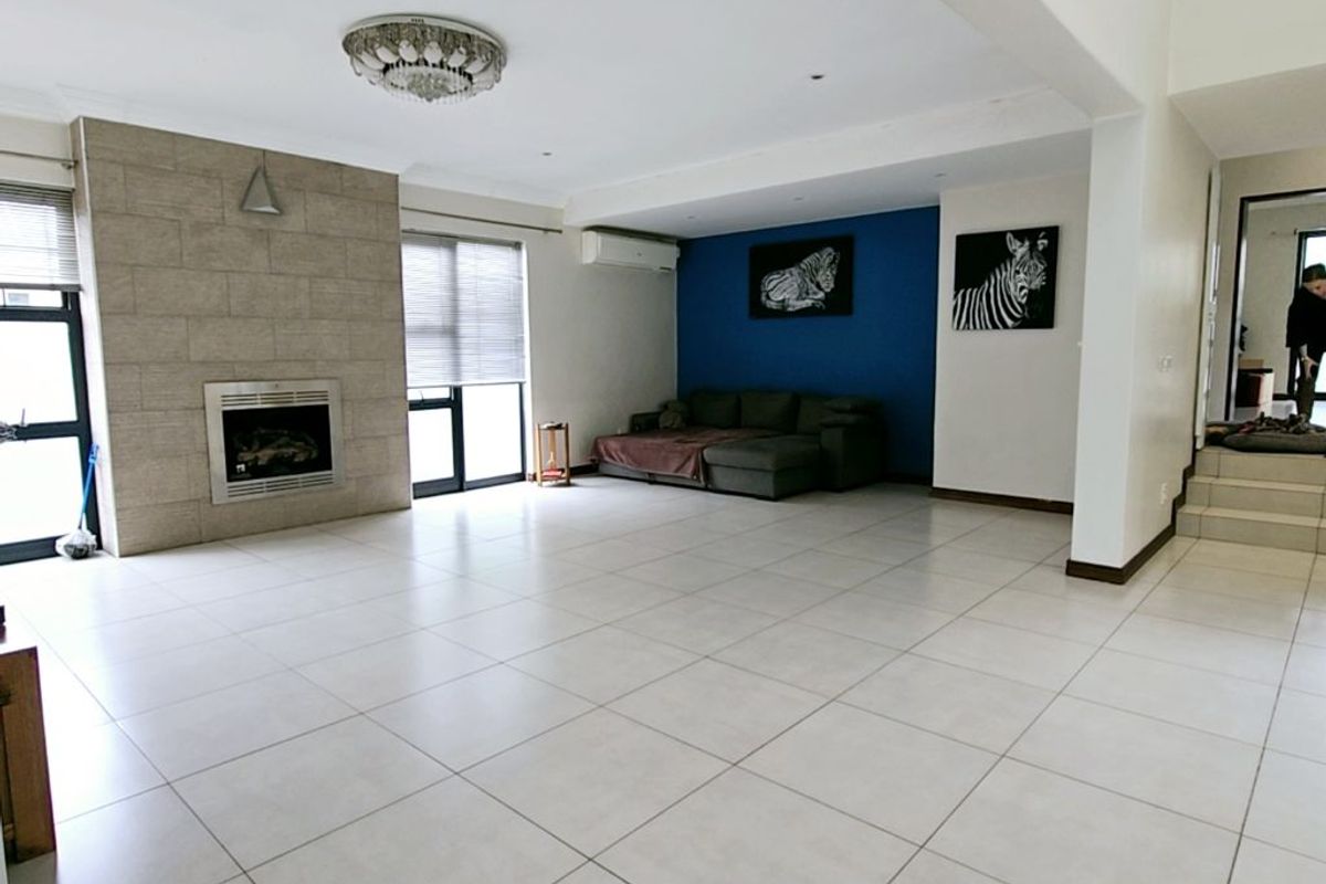 Spacious open-plan living area featuring large format floor tiles, a stone-clad fireplace, and a split-system air conditioning unit.