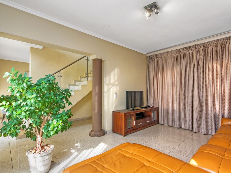 A spacious living area featuring tiled flooring, decorative columns, and an open staircase with a modern glass balustrade.